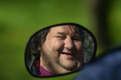 Reflection of happy man on rear-view mirror of car