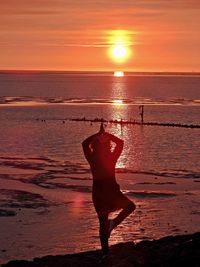 Silhouette woman exercising at beach during sunset