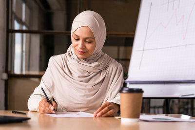 Young woman using mobile phone while sitting on table