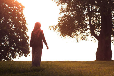 Rear view of woman standing on field against sky