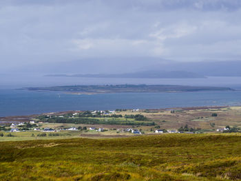 Scenic view of green landscape and sea against cloudy sky