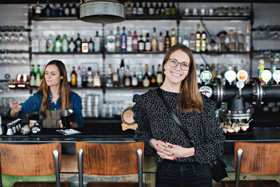 Portrait of smiling customer leaning at checkout counter with female owner in background