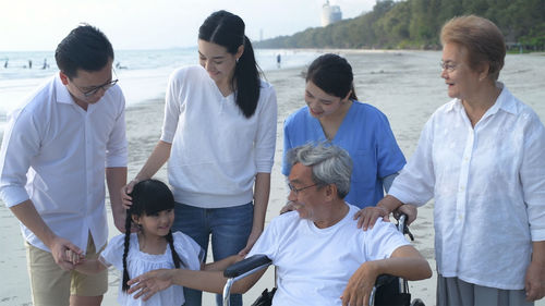 Senior man with family sitting on wheelchair at beach