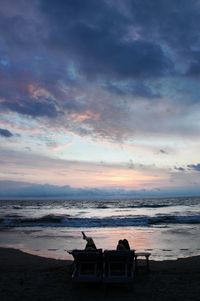 Chairs on beach against sky during sunset