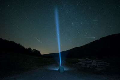 Rear view of man with illuminated flashlight sitting against star field at night