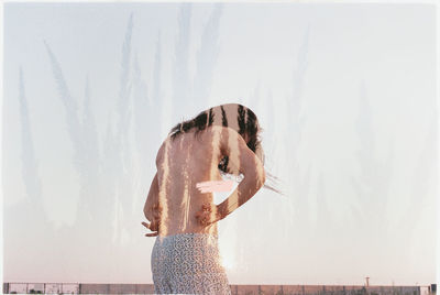 Double exposure of topless young woman and plants against sky
