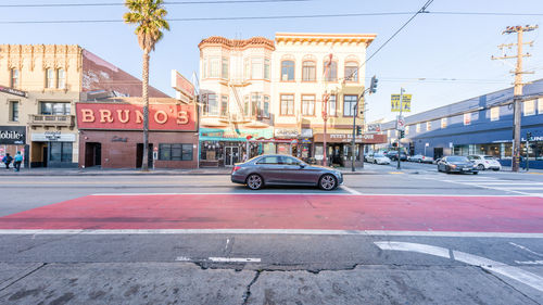 Cars on city street by buildings against sky