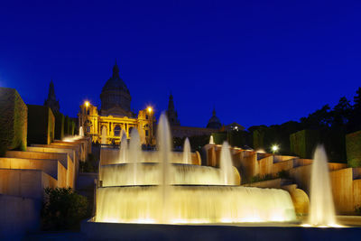 Illuminated buildings against clear blue sky at night