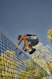 Low angle view of man jumping over net against clear sky