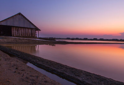 House by lake against sky during sunset