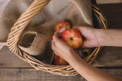 Cropped hands of woman holding apples in basket on table
