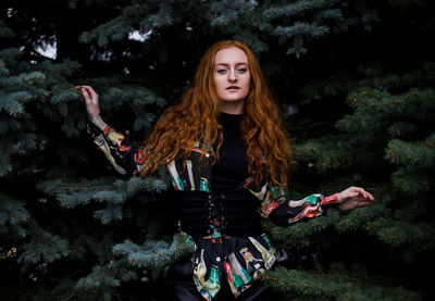 Portrait of young woman standing by trees at park