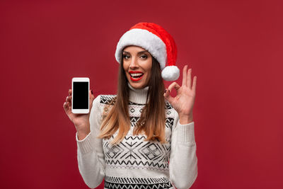 Portrait of smiling young woman using mobile phone against red wall