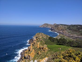 Scenic view of sea by cliff against clear blue sky