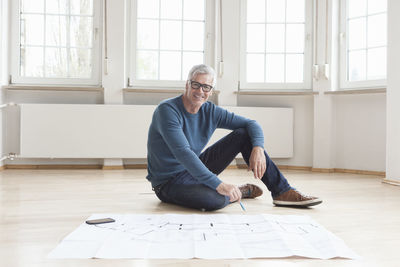 Portrait of smiling man with construction plan in empty apartment