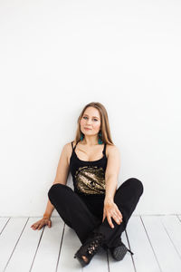 Portrait of a young woman sitting against white wall