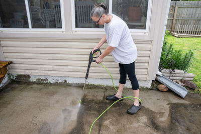 Woman pressure washes the algae growth from the patio and sidewalk