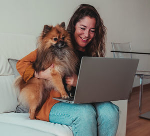 Smiling woman using laptop while sitting with dog at home