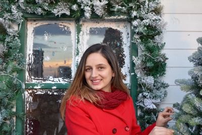 Portrait of smiling young woman standing against decorated window during winter