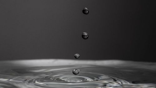 Close-up of drop falling on water against black background