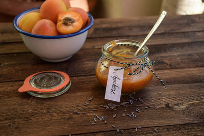 Apricot preserve with herb and bowl of apricots kept on wooden table