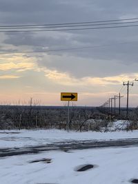 Road sign on snow covered field against sky