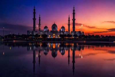 Reflection of illuminated mosque against sky during sunset