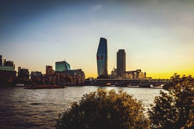 River by city buildings against sky during sunset