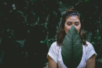 Portrait of young woman covering mouth with leaf against plants