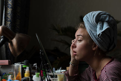 Profile view of young woman applying mascara at home