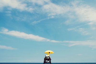 Person with umbrella on lookout tower at beach against sky