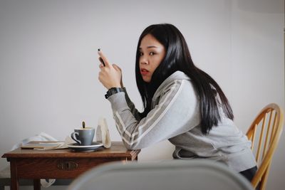 Side view portrait of young woman using phone while sitting in cafe