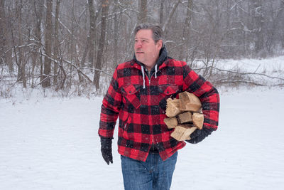 Midsection of mature man with wood during snowfall