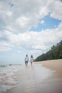 Man and woman walking at beach against sky