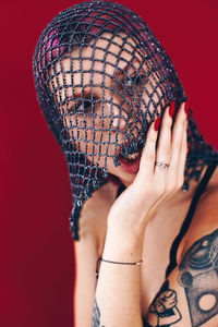 Close-up of young woman looking away while wearing net scarf against red background