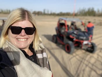 Portrait of woman wearing sunglasses in desert with dune buggy 
