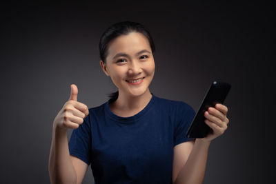 Portrait of smiling man holding smart phone against black background