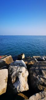 Rocks by sea against clear blue sky