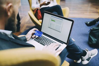 High angle view of businessman holding credit card while using laptop at airport