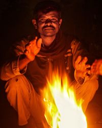 Portrait of man crouching by fire at night