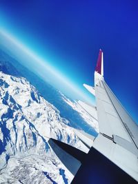 Airplane flying over snowcapped mountain against blue sky