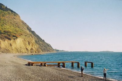 Rear view of man and woman standing on shore at beach against clear sky