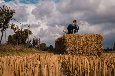 Girl climbing on hay bale against sky