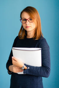 Portrait of beautiful young woman standing against blue background