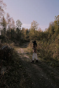 Woman standing amidst trees in forest against sky