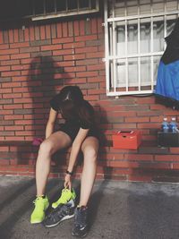 Full length of young woman sitting on brick wall