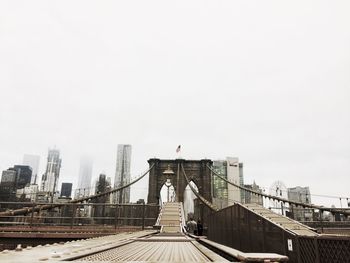 Suspension bridge in city against clear sky