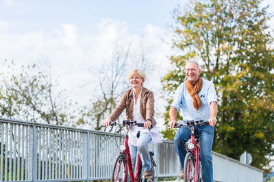 Smiling man with woman riding bicycles against trees