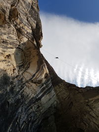 Low angle view of man climbing on rocky mountains against cloudy sky