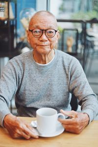 Portrait of senior man with coffee on table sitting in cafe